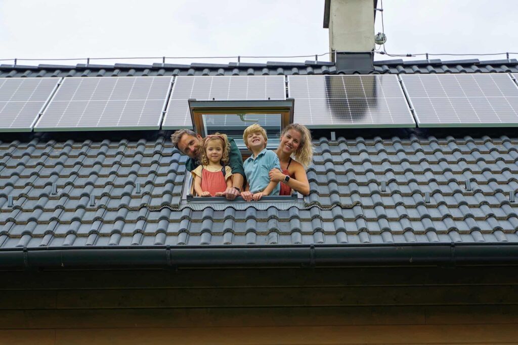 happy family leaning out from skylight window in their new house with solar panels on the roof